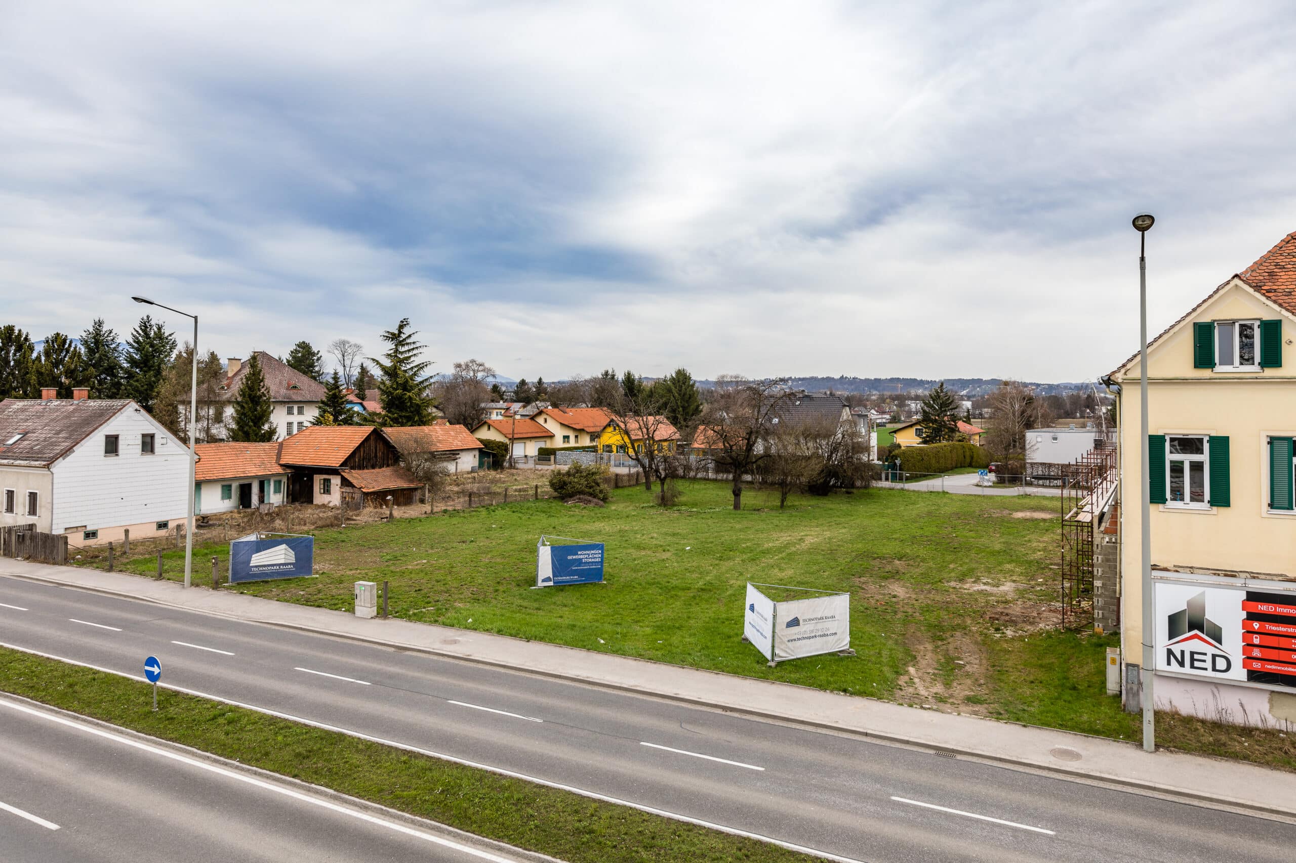 Straßenansicht mit freiem Baugrundstück und umliegenden Wohnhäusern in Triesterstraße, zusätzlicher Parkplatz daneben.