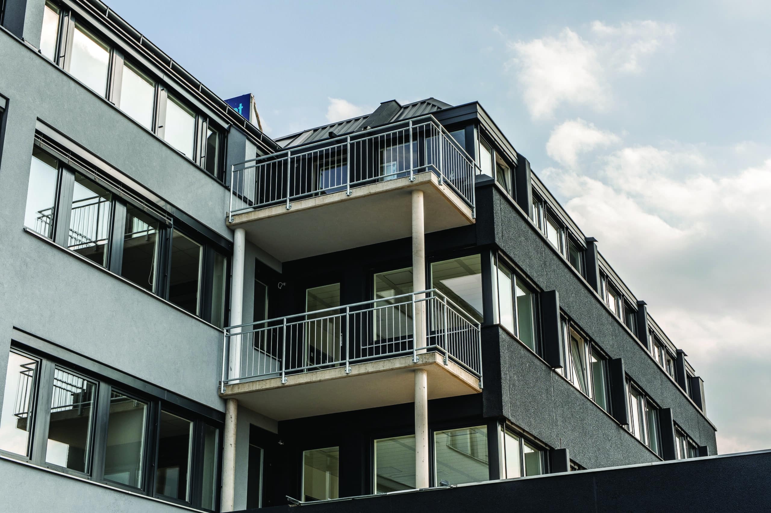Modernes Gebäude mit großen Fenstern und Balkonen bei bewölktem Himmel.