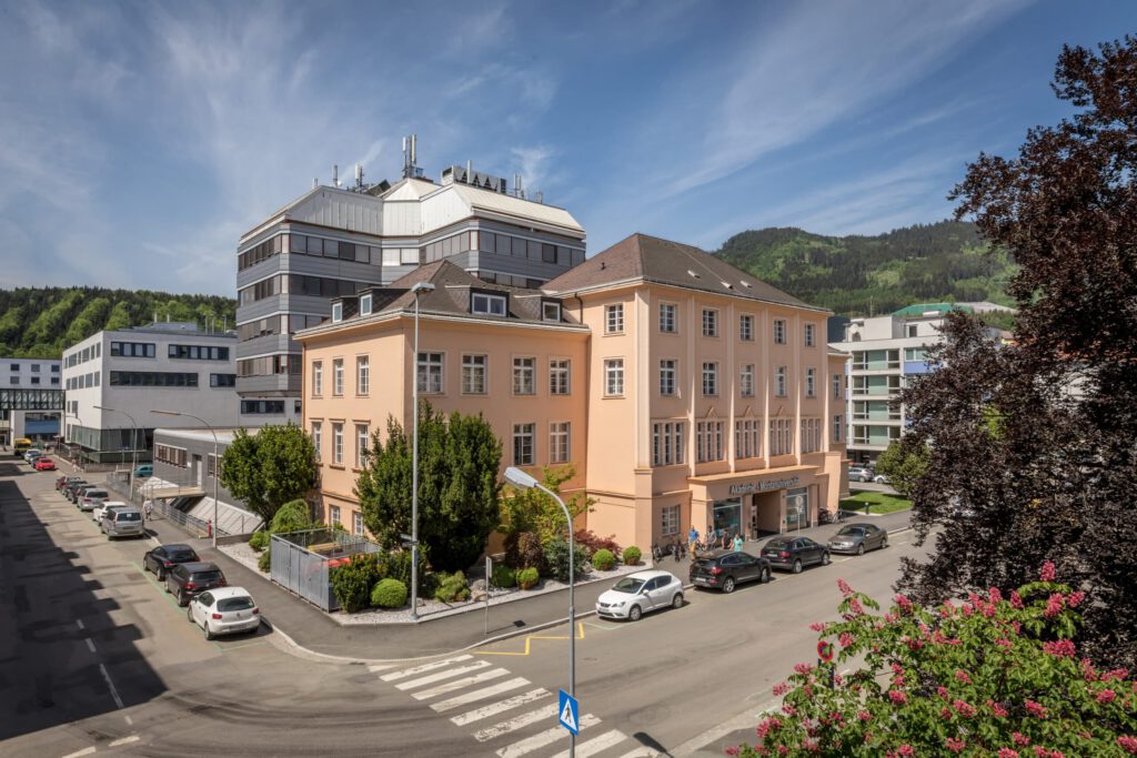 Helles Gebäude der Montanuniversität Leoben mit umliegenden Straßen und grüner Hügelkulisse.