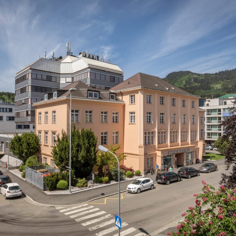 Helles Gebäude der Montanuniversität Leoben mit umliegenden Straßen und grüner Hügelkulisse.
