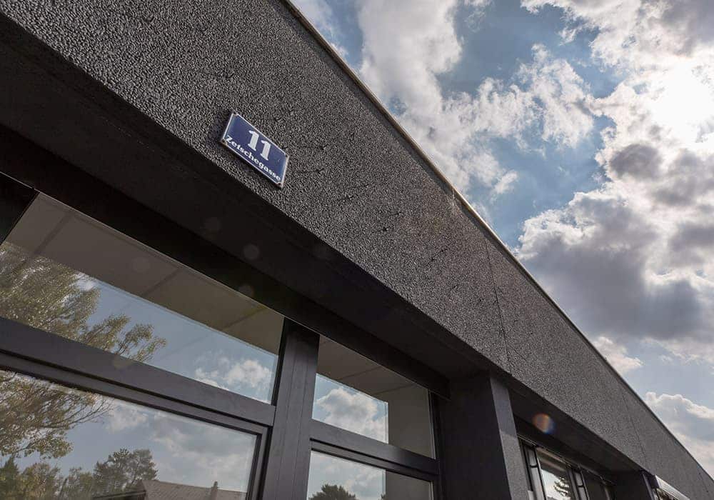 Moderne Gebäudefassade mit großem Fenster und Himmel im Hintergrund, Hausnummer 11 sichtbar.