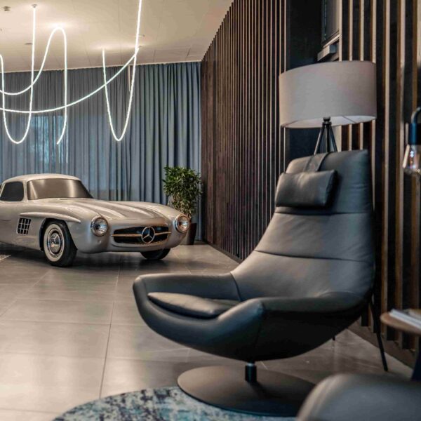 Moderner Wohnraum mit Ledersessel, Stehlampe und klassischem Auto im Hintergrund.