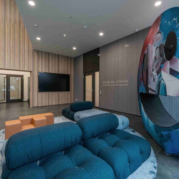 Moderne Lobby mit blauen Sofas, künstlerischer Wandgestaltung und Holzwand, gläserner Eingang.