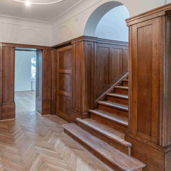 Holzverkleidete Treppe in einem historischen Gebäude mit Fischgrätenparkett.