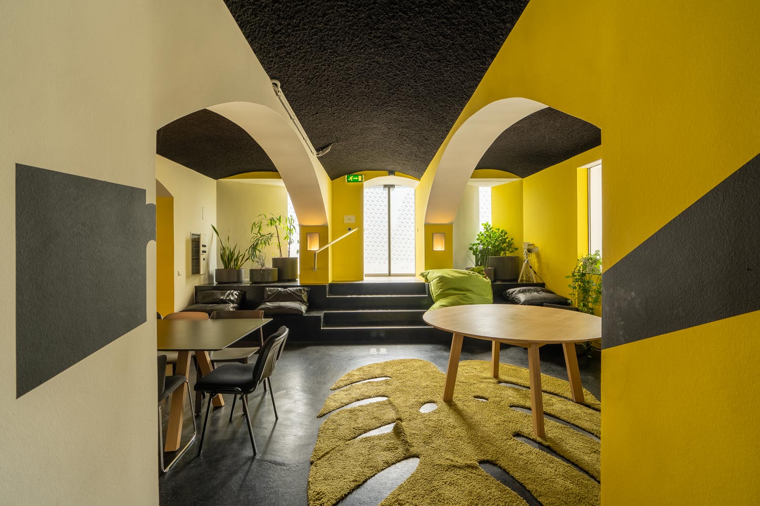 Modernes Wohnzimmer mit gelben Wänden, schwarzen Decken, Teppich, Pflanzen und Sitzbereich in Engelgasse 3-5.