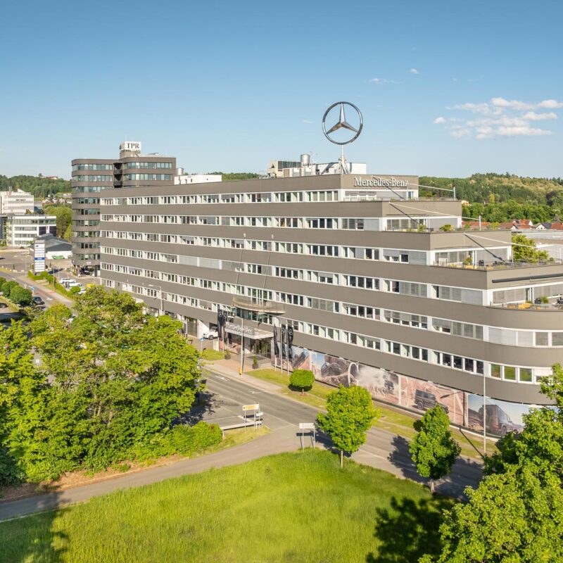 Technopark Raaba TP 2, modernes Bürogebäude mit Mercedes-Logo, umgeben von Grünflächen bei klarem Himmel.